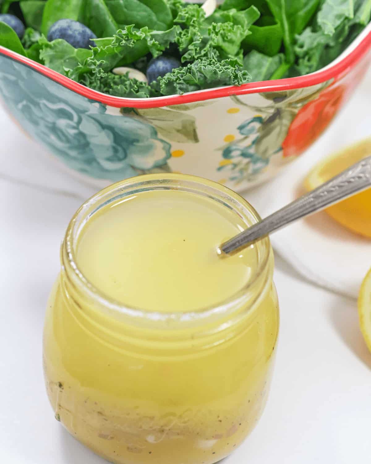 A jar of citrus vinaigrette next to a bowl of spinach and blueberries.