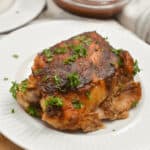 Crockpot roasted chicken on a white plate with BBQ sauce on the side.