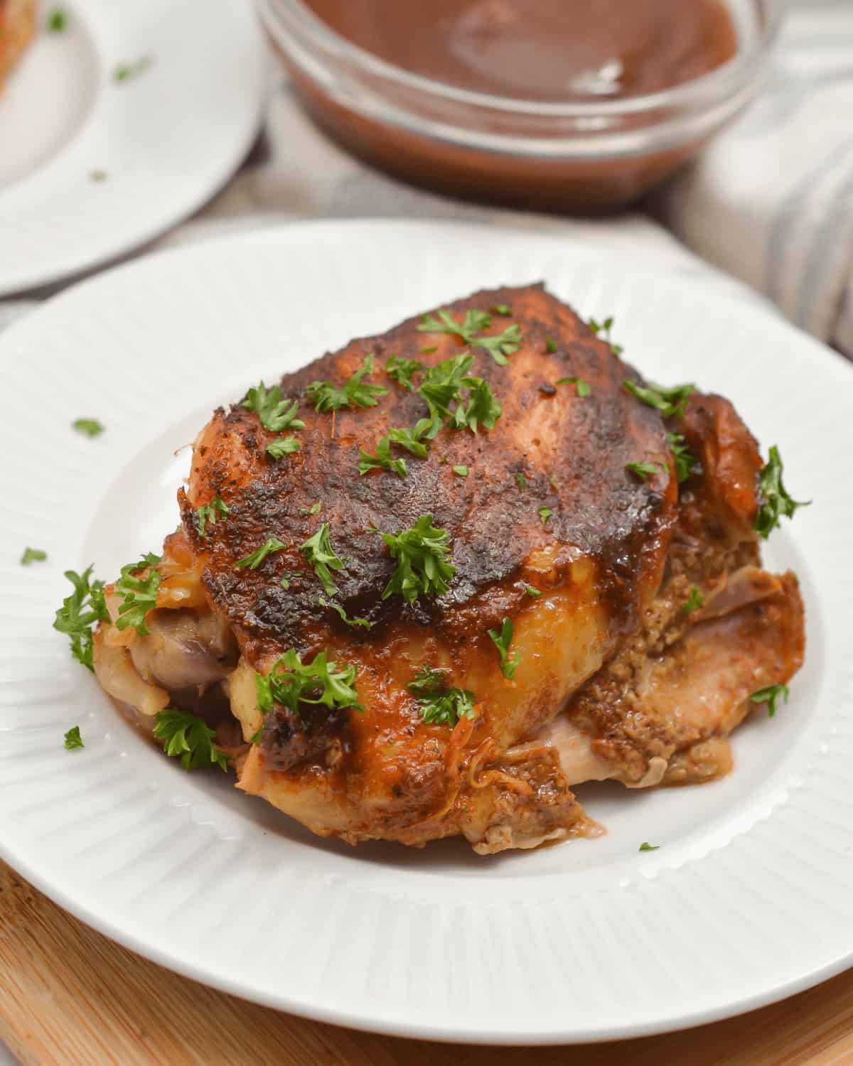 Crockpot roasted chicken on a white plate with BBQ sauce on the side.