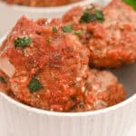 Italian sausage meatballs in a white bowl with sauce and parsley.
