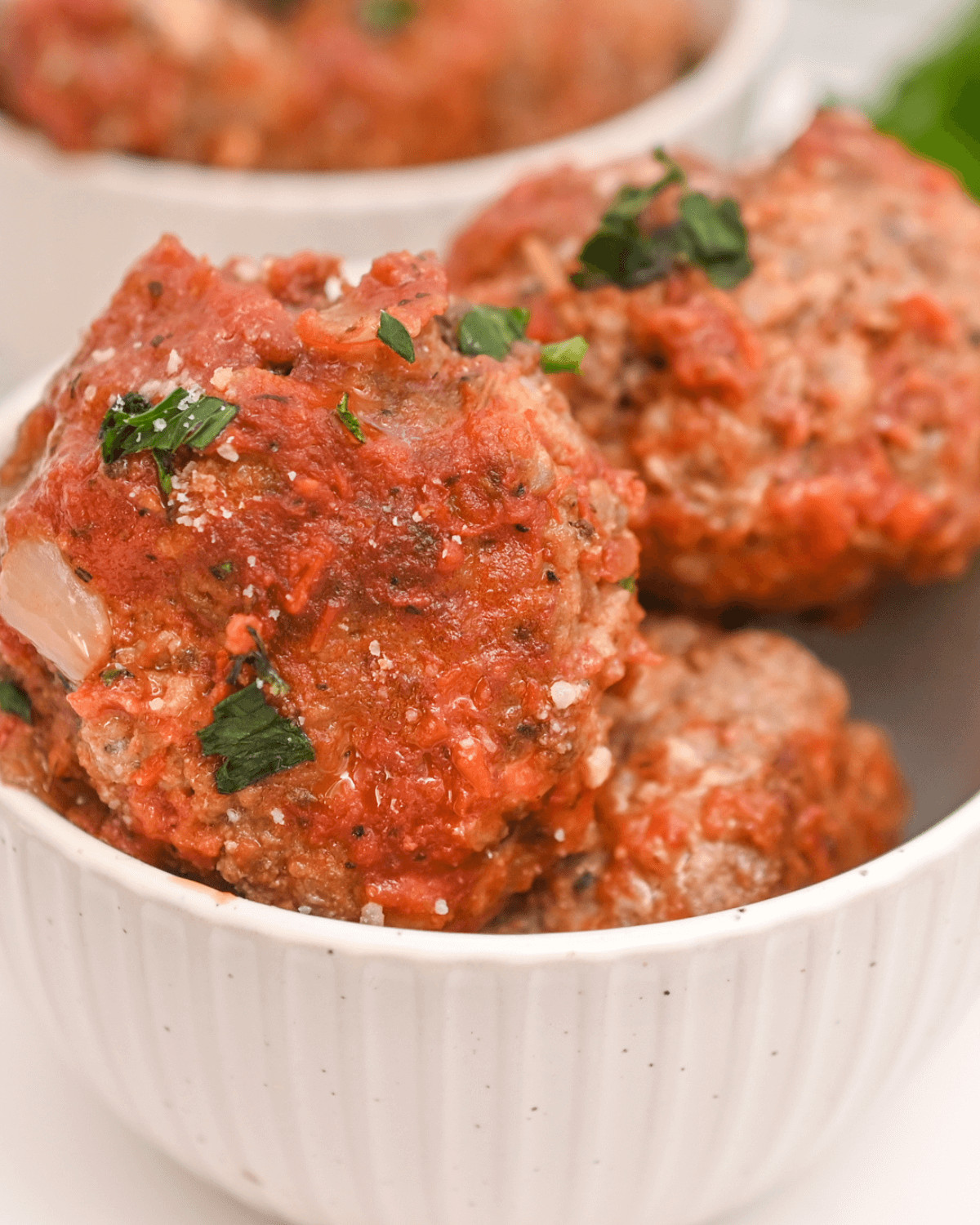 Italian sausage meatballs in a white bowl with sauce and parsley.