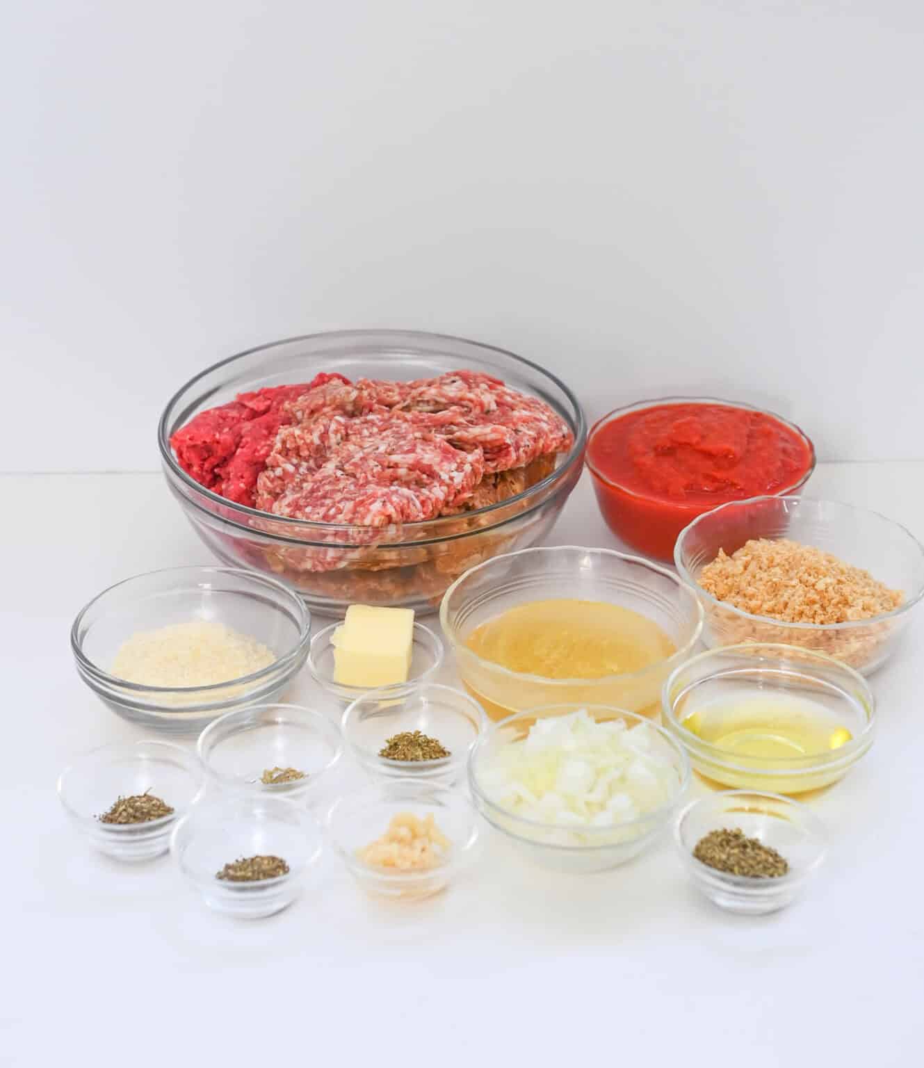 Italian sausage meatballs and other ingredients for a hamburger are shown in bowls on a white background.