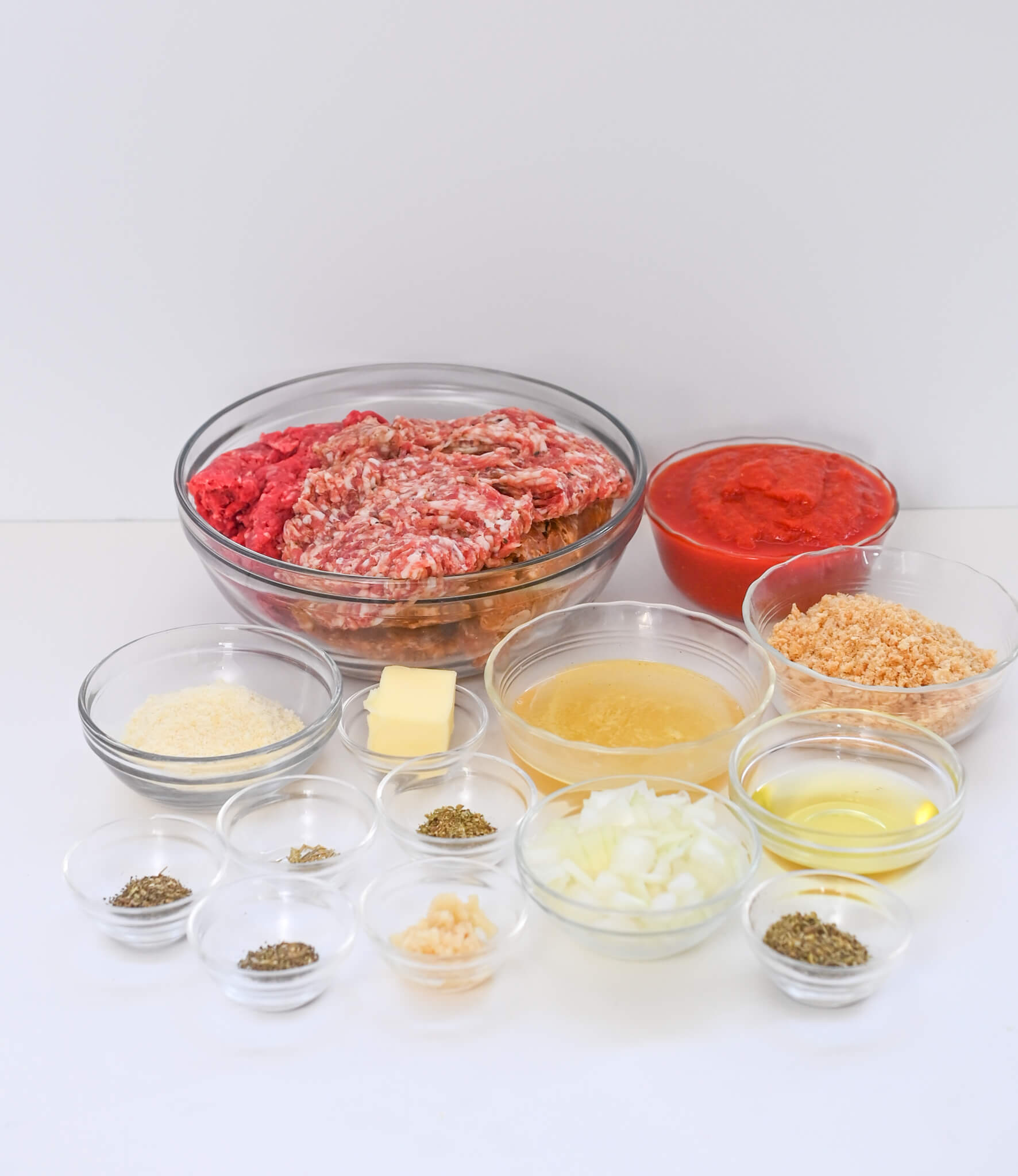 Italian sausage meatballs and other ingredients for a hamburger are shown in bowls on a white background.