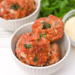 A bowl of Italian sausage meatballs with sauce and parmesan.