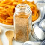 A glass jar of French fry seasoning next to a wooden spoon.