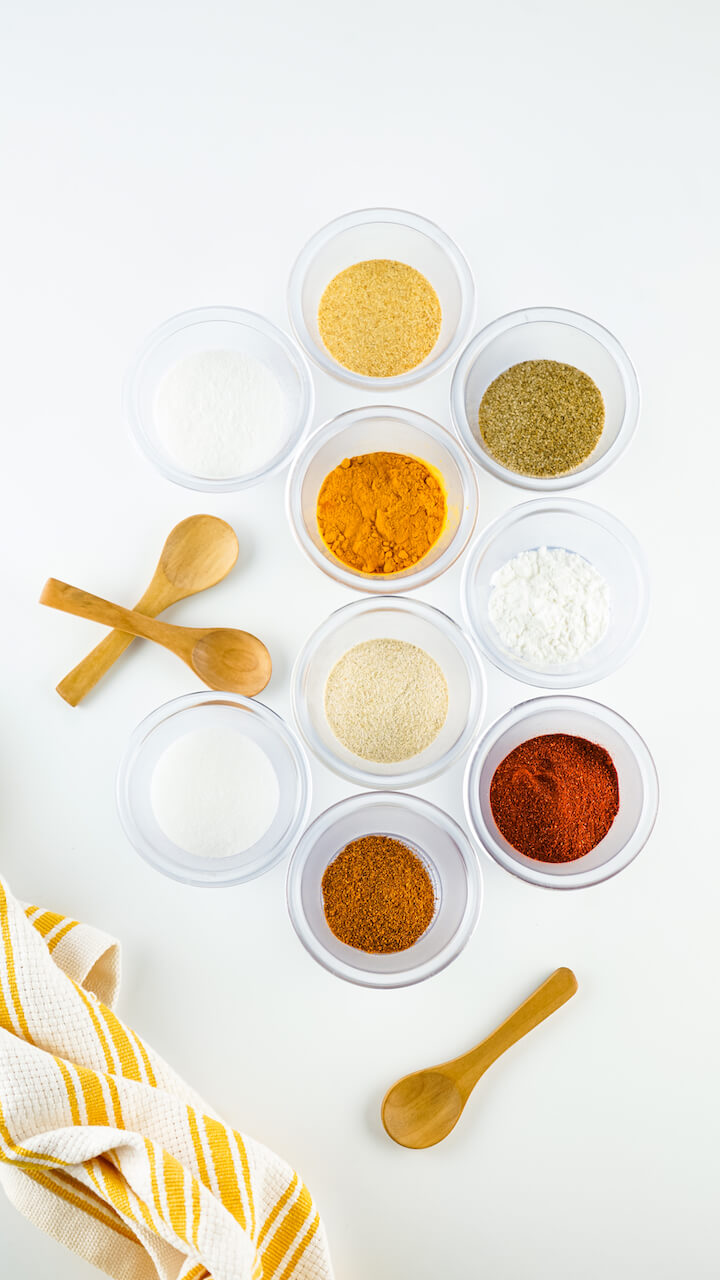 Assorted spices in small bowls on a white backdrop.