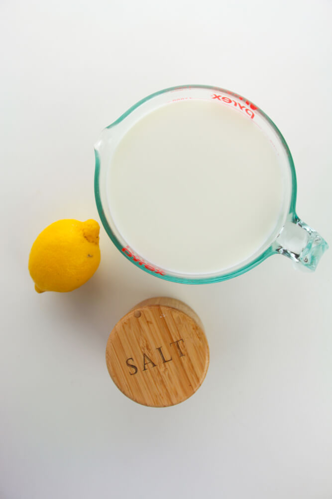 A measuring cup milk with a lemon and salt next to it, showing the essential ingredients for making ricotta cheese.