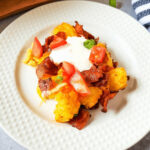 A plate with bacon, tomatoes and sour cream, loaded with tater tots.