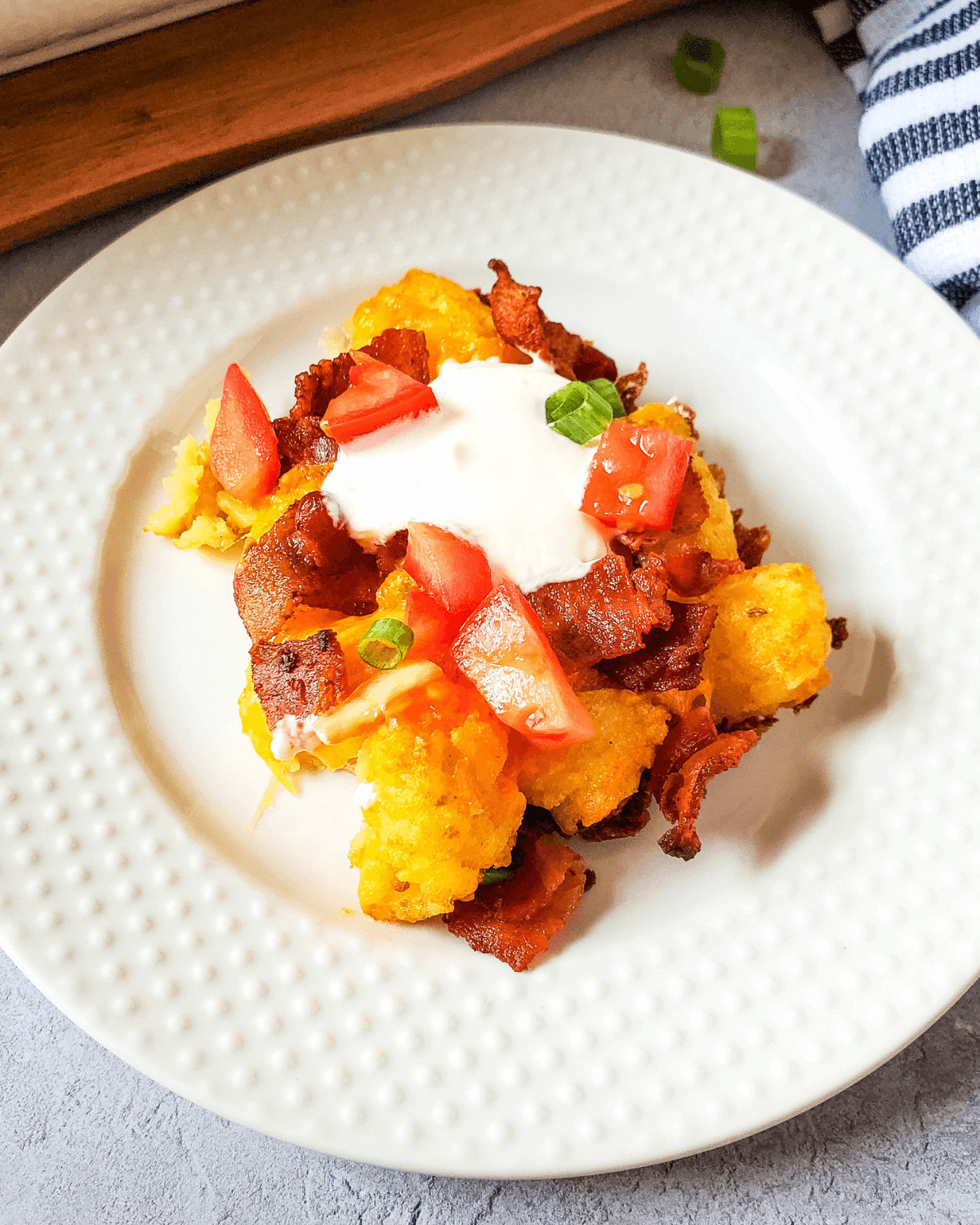 A plate with bacon, tomatoes and sour cream, loaded with tater tots.
