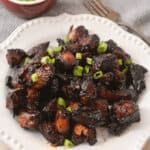 A white plate with a plate of burnt ends on it.