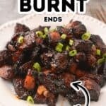 A plate of dark, glazed Pork Burnt Ends garnished with chopped green onions, served on a white dish.