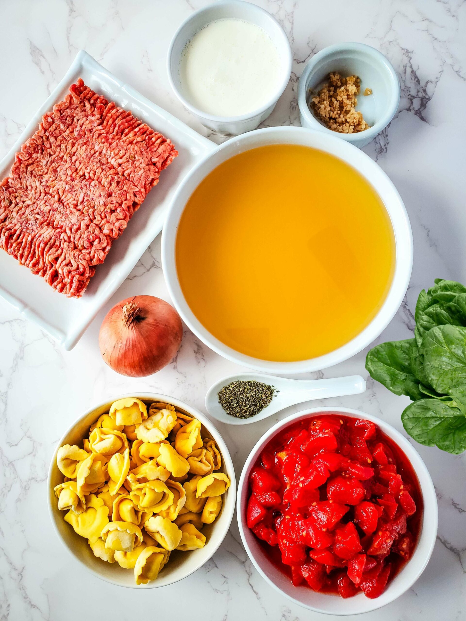 Ingredients for Sausage and Spinach meatballs in a white bowl on a marble countertop.