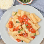 Slow-roasted tomato basil pasta served on a white plate with additional cheese and basil on the side.