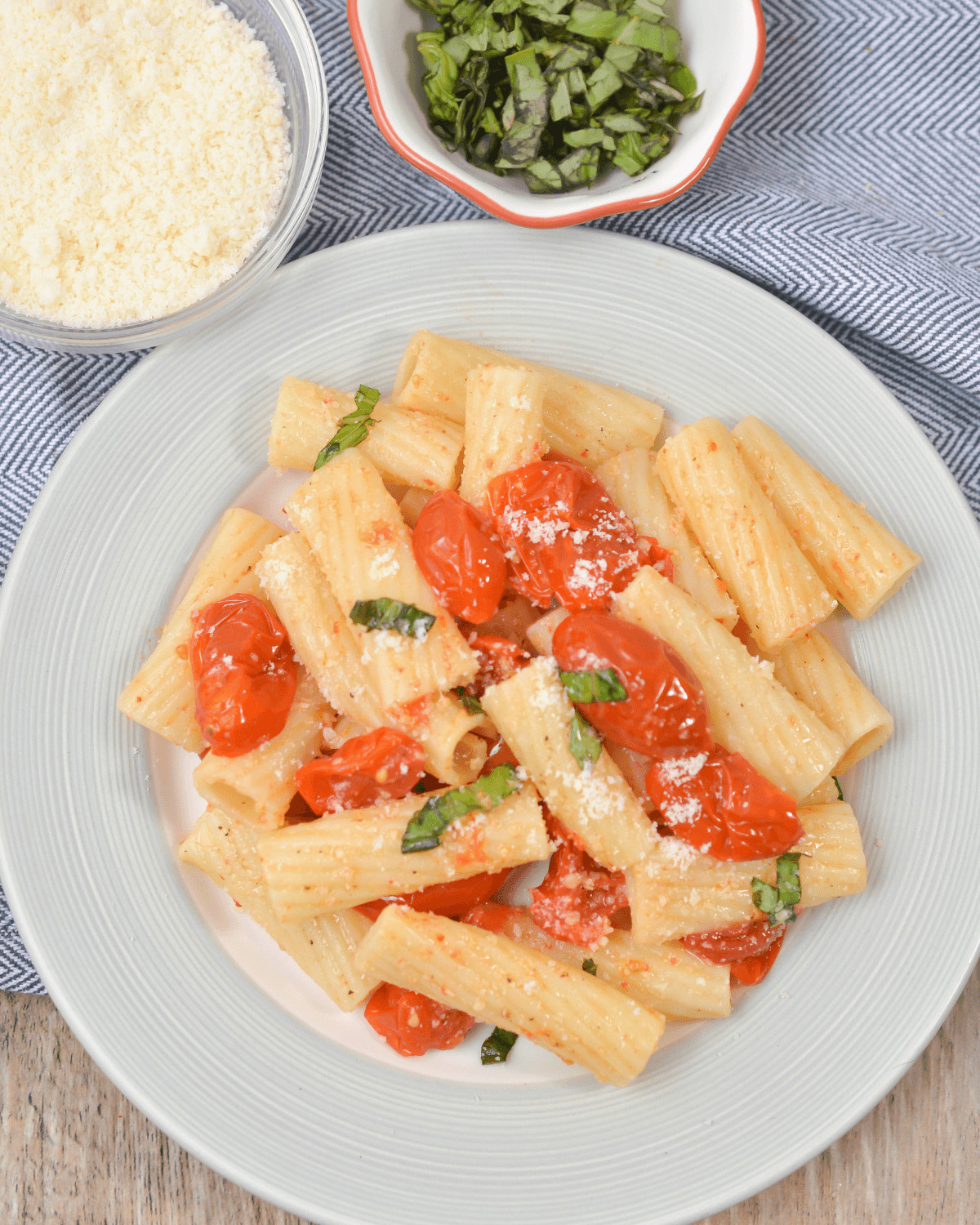 Slow-roasted tomato basil pasta served on a white plate with additional cheese and basil on the side.