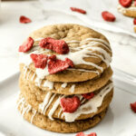 A stack of strawberry cookies with icing and strawberries on a plate.