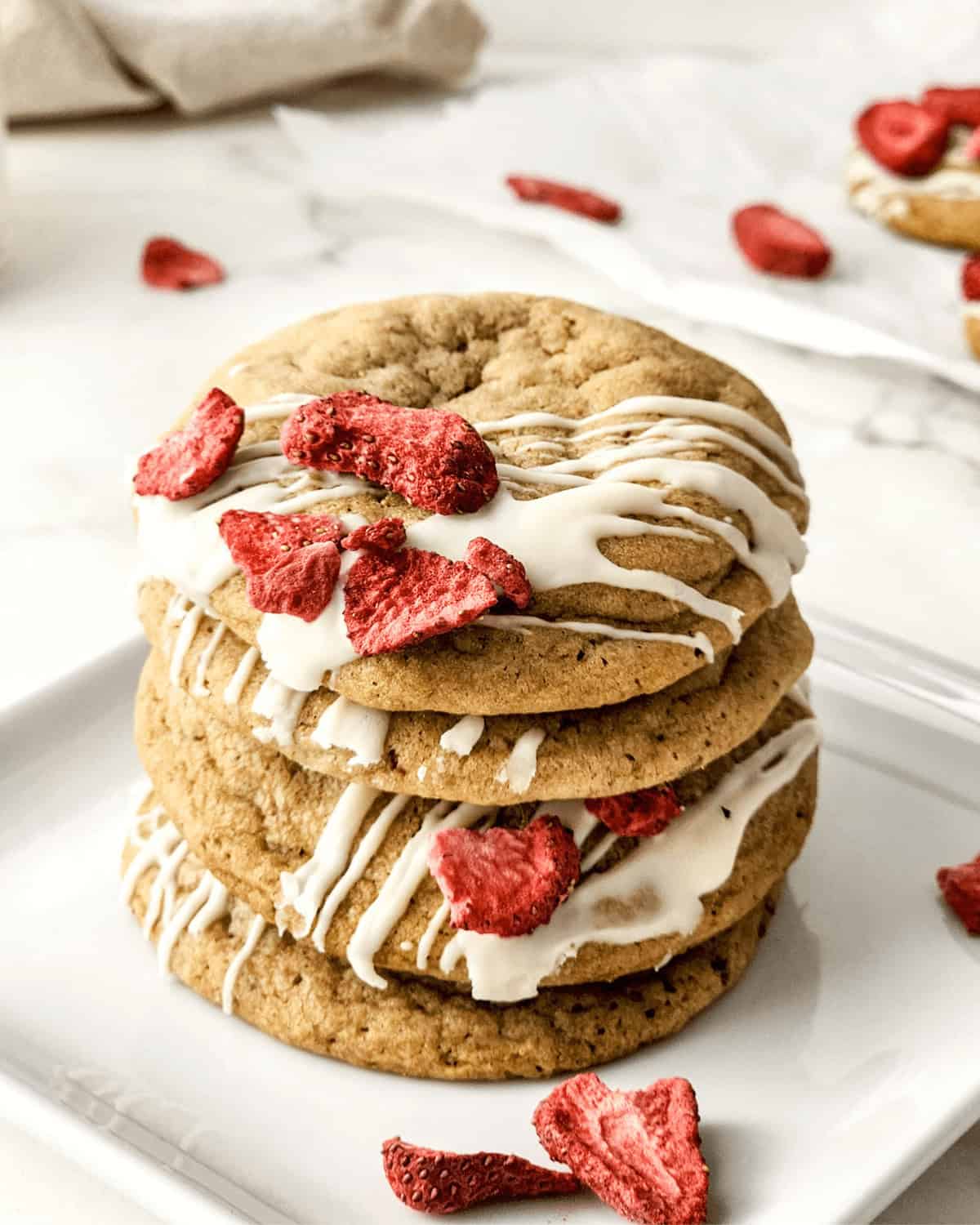 A stack of strawberry  cookies with icing and strawberries on a plate.