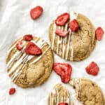Two strawberry cheesecake cookies with icing on a piece of paper.