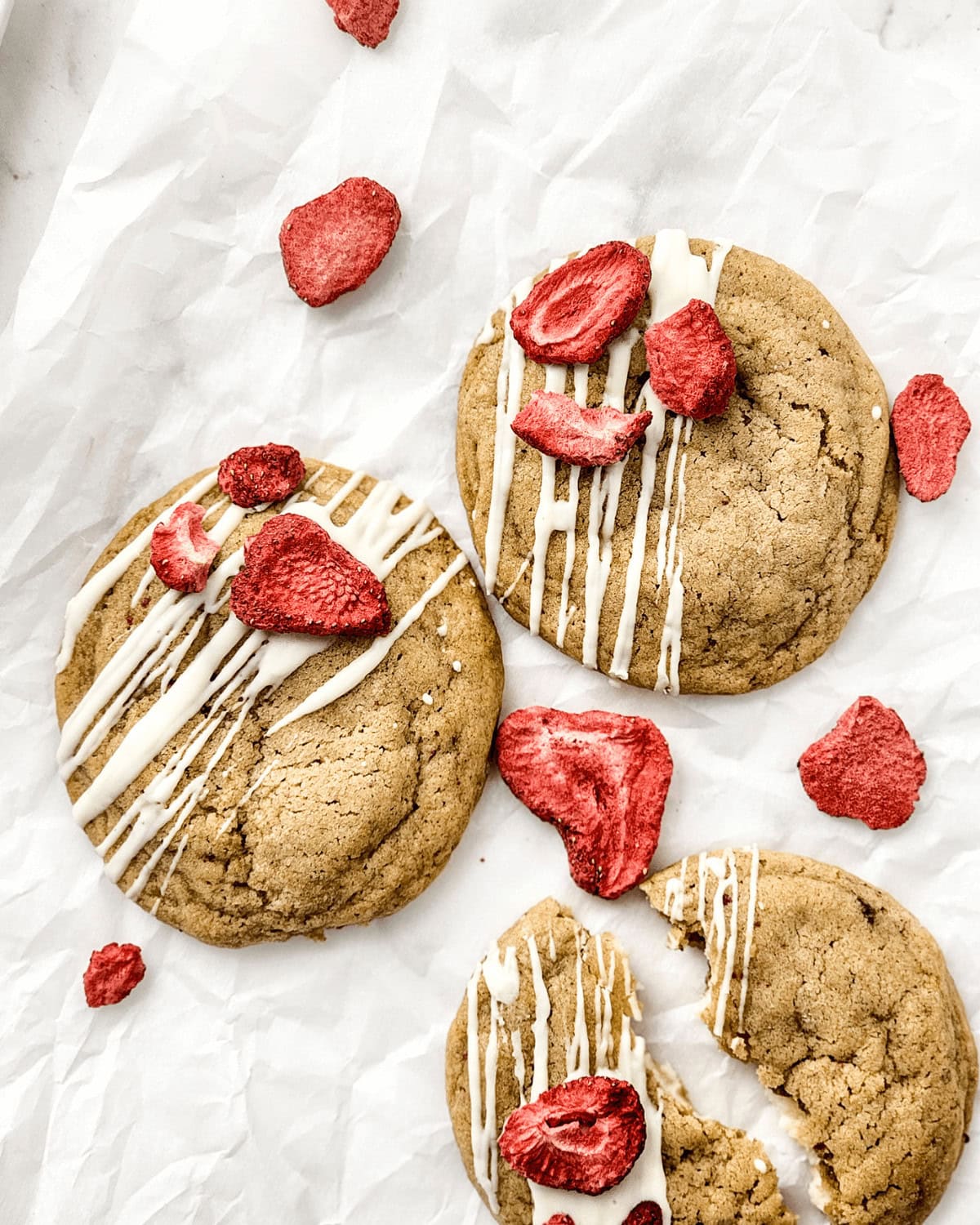 Two strawberry cheesecake cookies with icing on a piece of paper.
