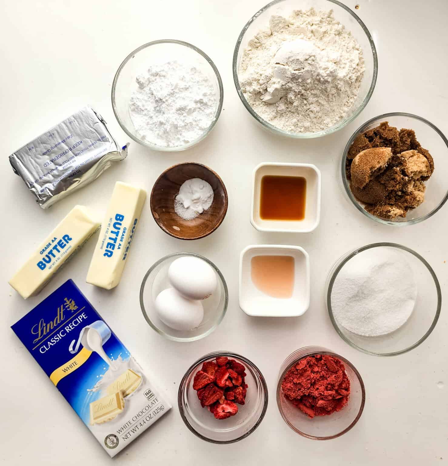 The ingredients for a are laid out on a white table. Including sugar, flour, dried strawberries and eggs.