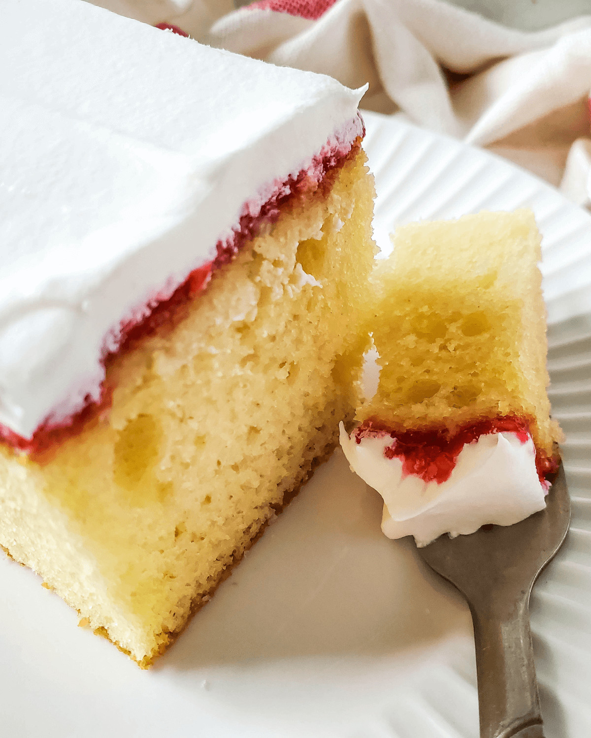 A slice of vanilla raspberry cake on a plate with a fork.