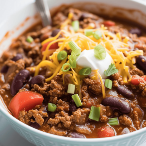 Venison chili in a white bowl topped with sour cream and cheese.