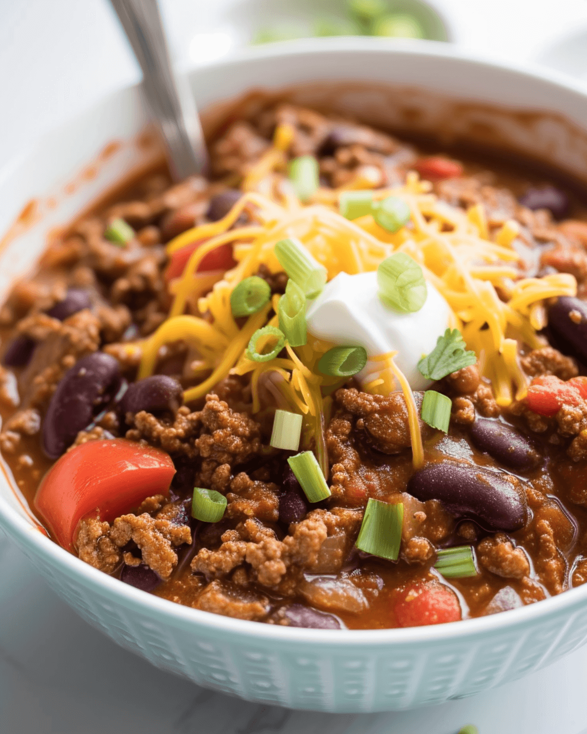 Venison chili in a white bowl topped with sour cream and cheese.