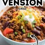 Bowl of hearty venison chili, made from a flavorful venison chili recipe and topped with shredded cheese, sour cream, and chopped green onions, with visible kidney beans and tomatoes.
