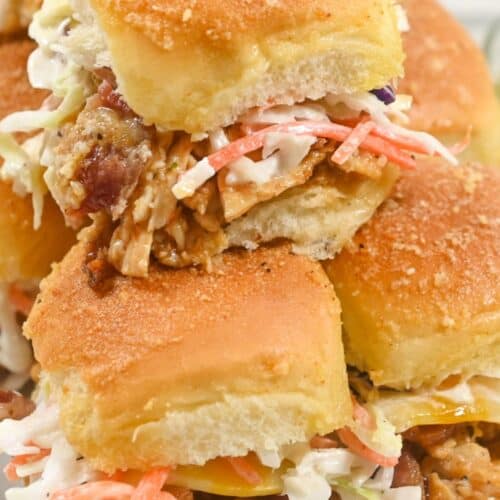 A close-up of stacked BBQ Chicken Sliders with coleslaw and cheese on soft, golden buns.