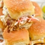 A close-up of three mouthwatering sandwiches with coleslaw, stacked on top of each other, on a white plate.