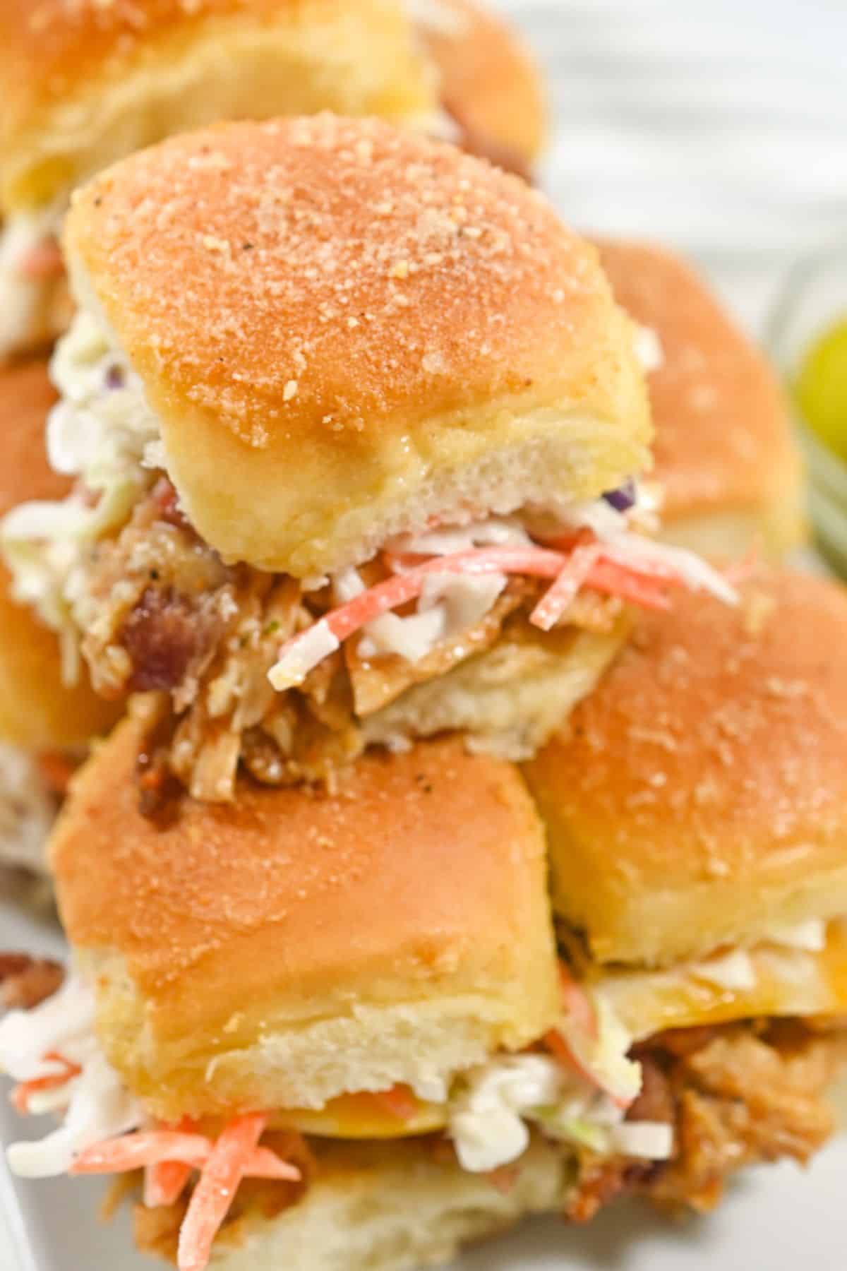 A close-up of three mouthwatering sandwiches with coleslaw, stacked on top of each other, on a white plate.