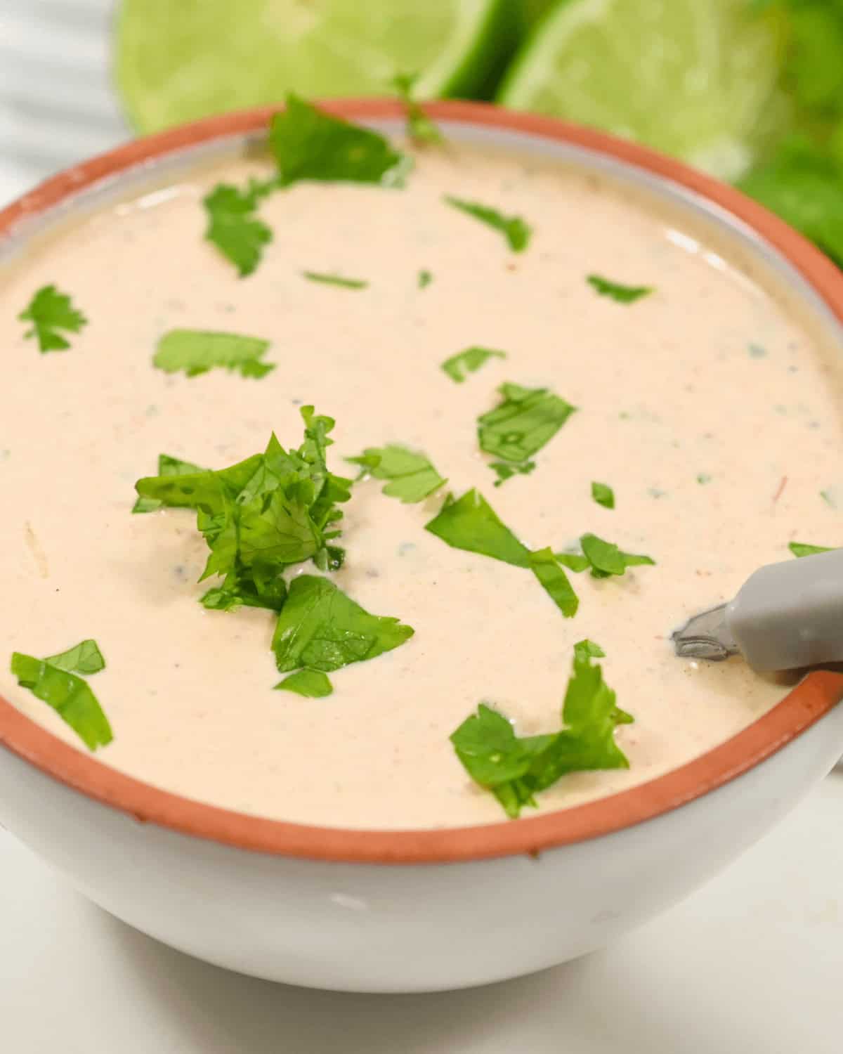 A bowl with Baja Chipotle Sauce and lime wedges in the background.