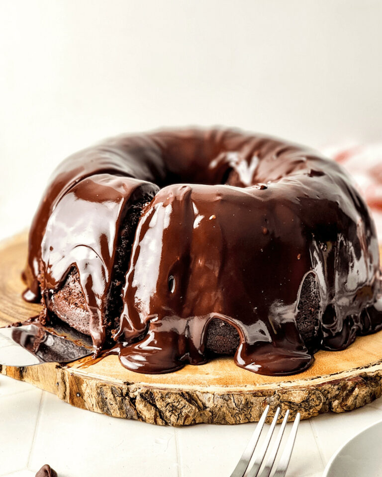 Chocolate chip bundt cake with glossy ganache on a wooden serving board.