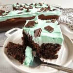 A chocolate mint cake with mint green frosting and topped with chocolate pieces, partially served on a plate.