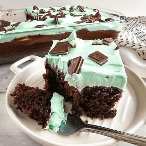 A chocolate mint cake with mint green frosting and topped with chocolate pieces, partially served on a plate.