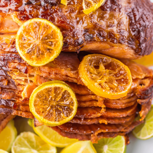 Glazed crock pot spiral ham topped with caramelized citrus slices, surrounded by fresh lime wedges.