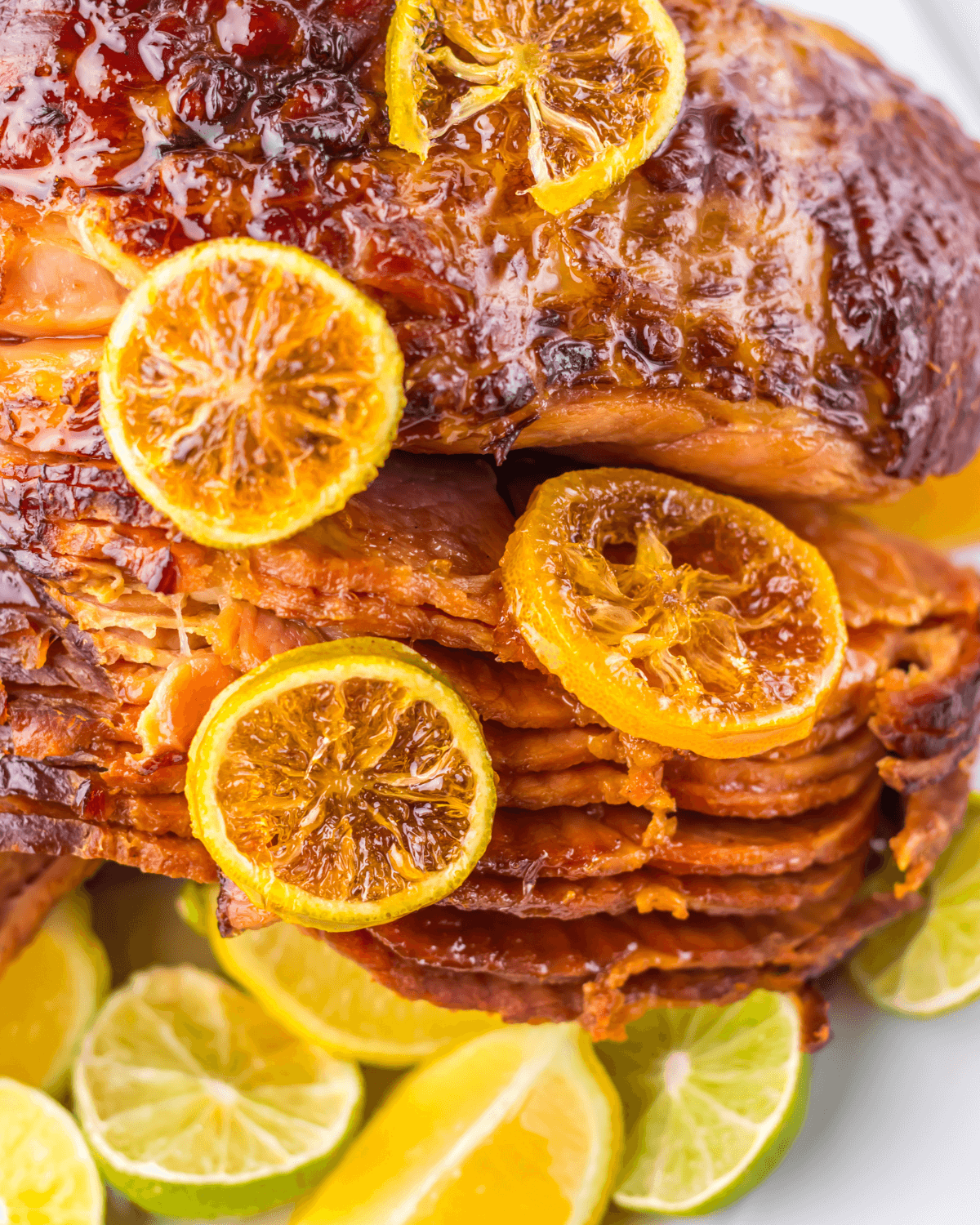 Glazed crock pot spiral ham topped with caramelized citrus slices, surrounded by fresh lime wedges.
