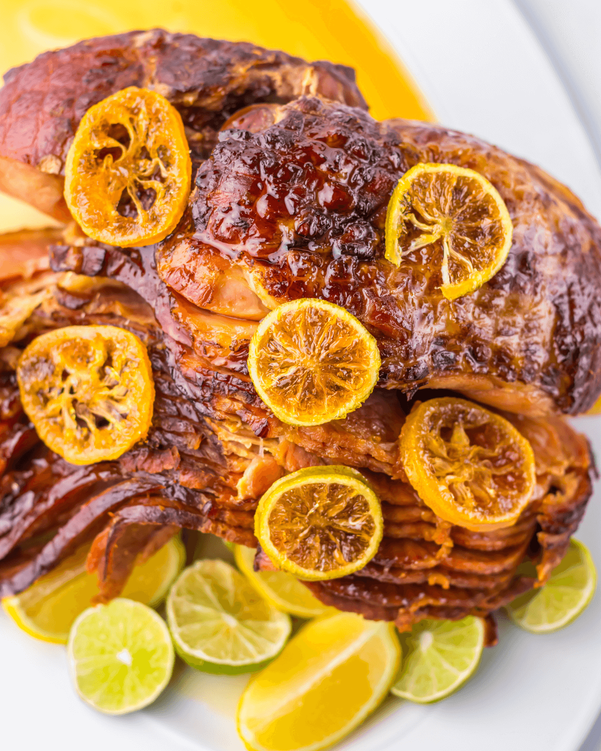 Meat with caramelized orange slices, accompanied by lime and orange wedges on a white plate.