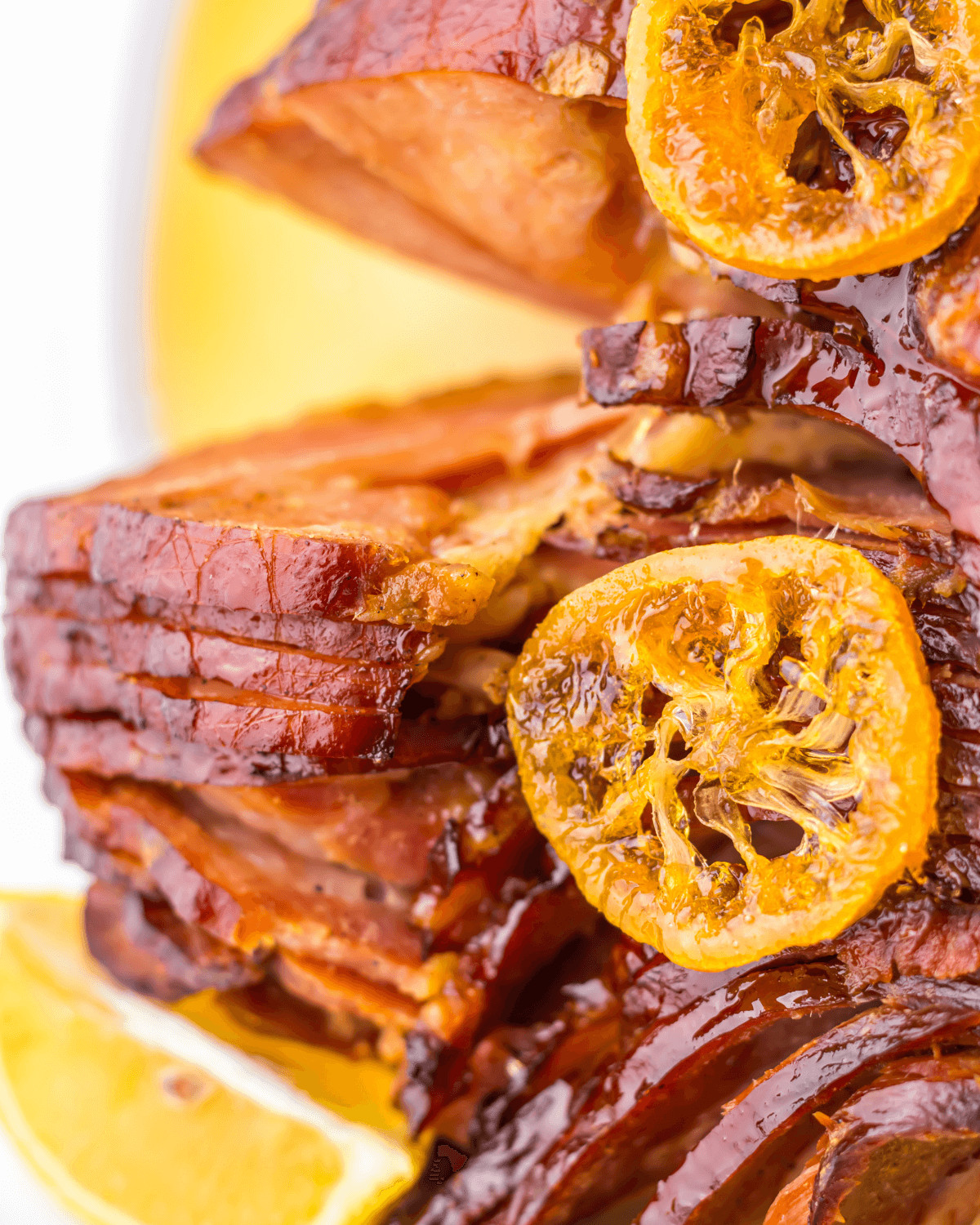 Stacked crock pot spiral honey-glazed ham slices garnished with caramelized orange slices.
