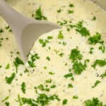 Creamy garlic parmesan sauce with chopped parsley and a gray ladle in a pot.
