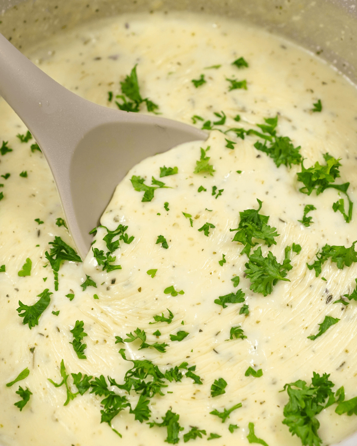 Creamy garlic parmesan sauce with chopped parsley and a gray ladle in a pot.