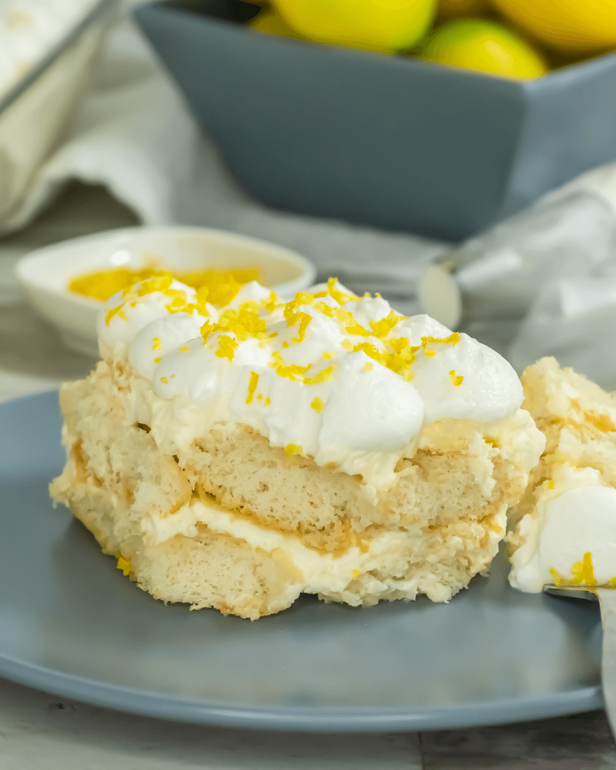 A slice of Limoncello Tiramisu with cream topping and lemon zest on a plate.