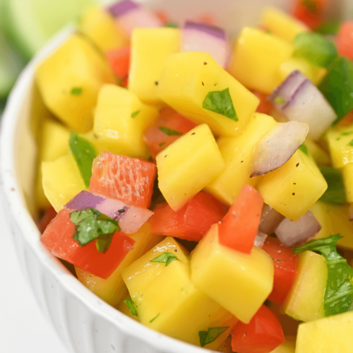 A colorful bowl of fresh mango habanero salsa with red onion and herbs.