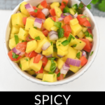 A bowl of mango habanero salsa garnished with lime, surrounded by fresh ingredients.
