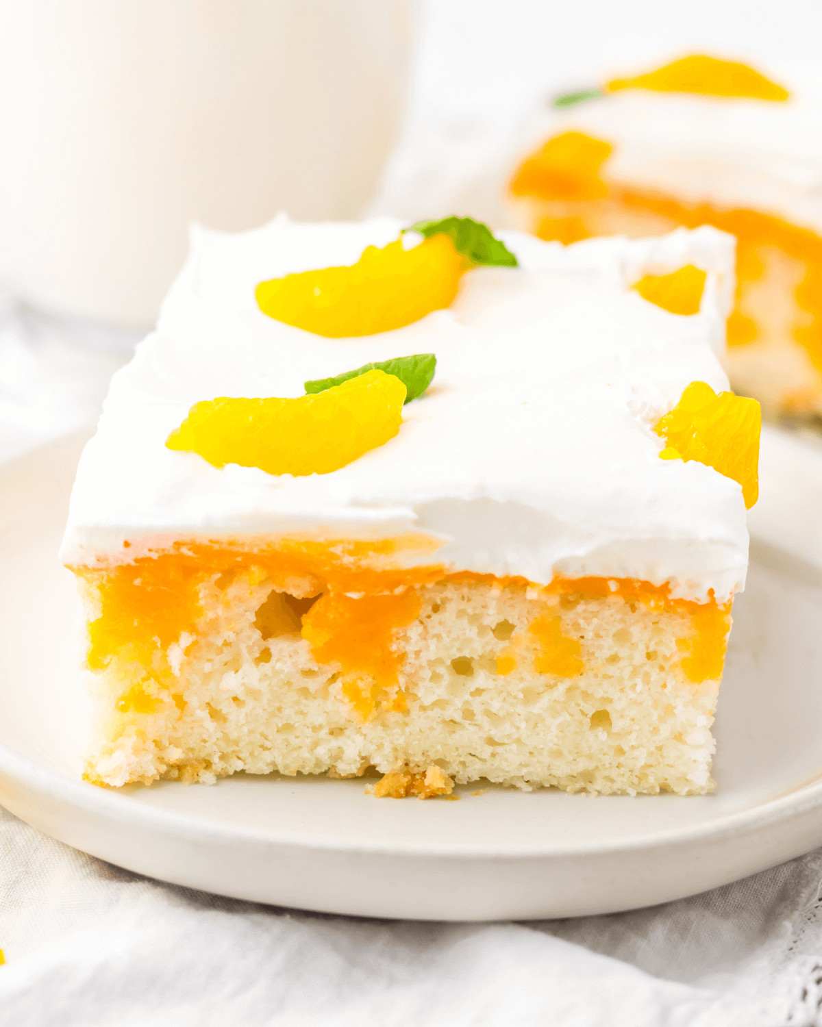 A slice of orange creamsicle cake with whipped cream topping and fruit garnish on a white plate.
