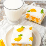 Two slices of dessert topped with whipped cream and orange segments, served with a glass of milk.