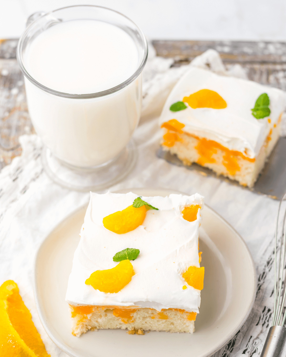 Two slices of dessert topped with whipped cream and orange segments, served with a glass of milk.