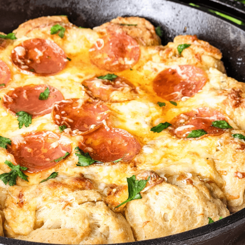 Pepperoni pizza dip bubble up bake in a cast-iron skillet, garnished with fresh parsley.