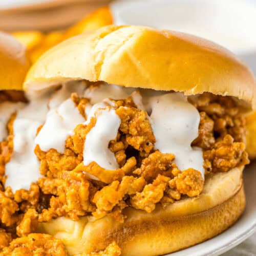 Slow cooker buffalo chicken sloppy joe sandwich on a bun, topped with sauce.