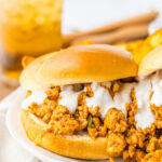 A slow cooker buffalo chicken sloppy joe sandwich with sauce on a bun, served with a side of fries and a glass of iced tea.