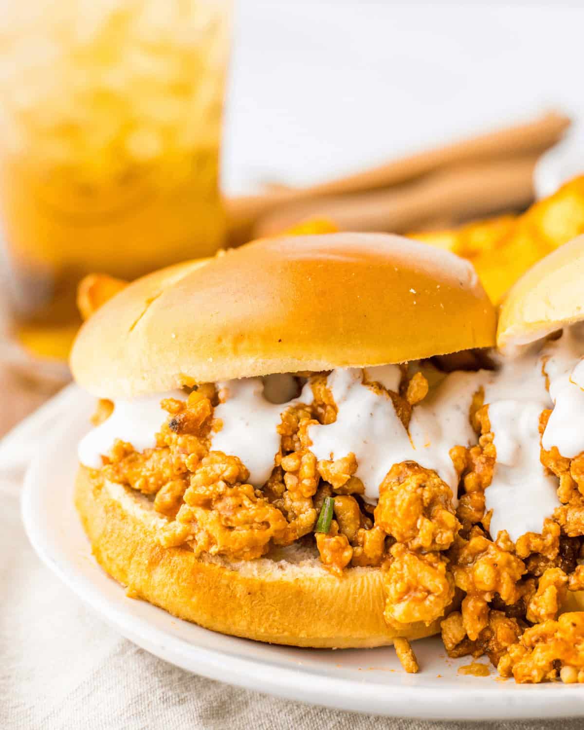 A sandwich with sauce on a bun, served with fries and a drink in the background.
